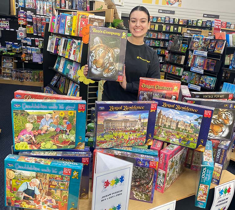 Woman holding a puzzle box in a store with various puzzle boxes displayed on a table.